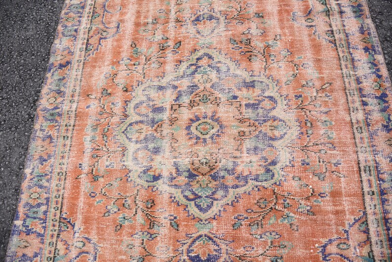 May include: A vintage rug with a faded peach background and a central medallion in shades of blue, green, and cream. The rug has a distressed look with a worn and faded appearance.