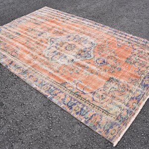 May include: A vintage rug with a faded peach background and a floral pattern in shades of blue, green, and cream. The rug has a fringed edge.