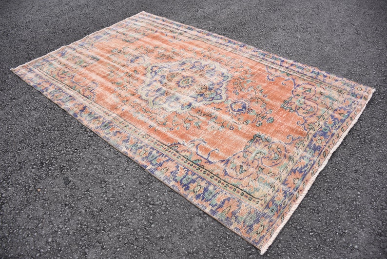 May include: A vintage rug with a faded peach background and a floral pattern in shades of blue, green, and cream. The rug has a fringed edge.