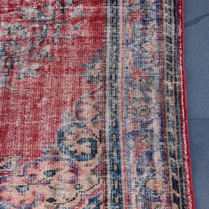 May include: Close-up of a red and blue vintage rug with a faded floral pattern. The rug has a distressed look and is made of a woven material.