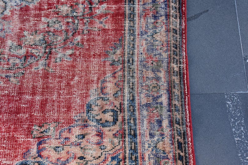 May include: Close-up of a red and blue vintage rug with a faded floral pattern. The rug has a distressed look and is made of a woven material.