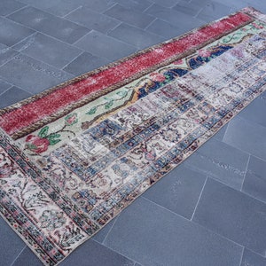 Puede incluir: Una alfombra de pasillo vintage con un dise&ntilde;o de patchwork en rojo, verde, azul y blanco. La alfombra tiene un patr&oacute;n floral y un aspecto descolorido y desgastado.