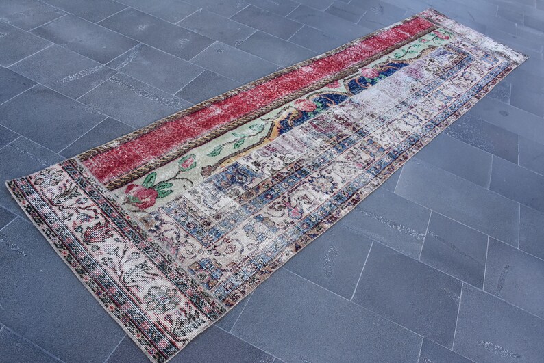 Puede incluir: Una alfombra de pasillo vintage con un dise&ntilde;o de patchwork en rojo, verde, azul y blanco. La alfombra tiene un patr&oacute;n floral y un aspecto descolorido y desgastado.