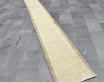 May include: A long, rectangular rug with a beige center and a brown border. The rug is placed on a dark gray tiled surface and appears to be made of a woven material. The rug's edges show some wear.