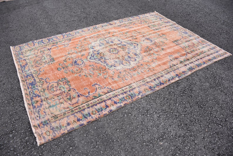 May include: A vintage rug with a peach background and a floral pattern in shades of blue, green, and white. The rug has a faded, distressed look, giving it a unique and antique feel.