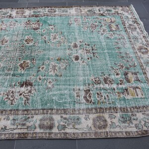 May include: A large, rectangular, distressed turquoise rug with a floral pattern. The rug features a central design with faded brown and cream-colored floral motifs. The border has a repeating pattern in similar colors. The rug is suitable for living rooms and bedrooms.