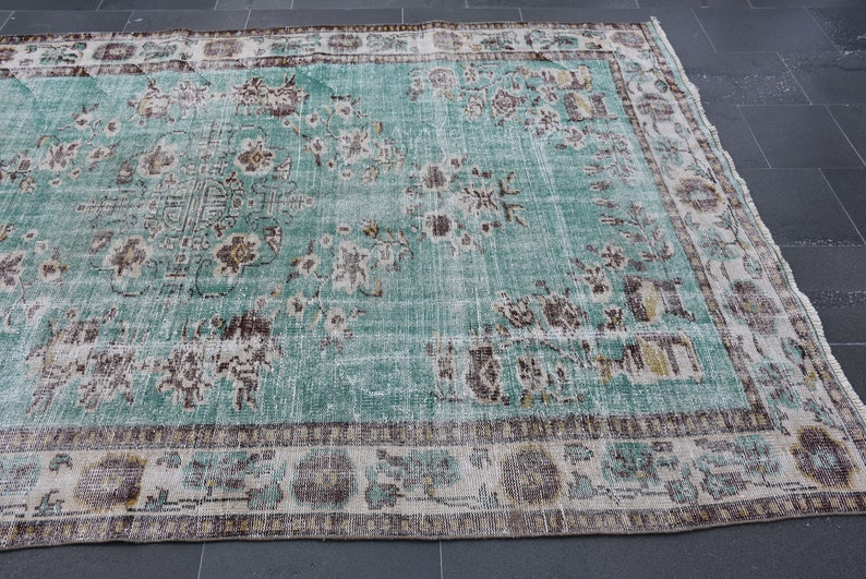May include: A large, rectangular, distressed turquoise rug with a floral pattern. The rug features a central design with faded brown and cream-colored floral motifs. The border has a repeating pattern in similar colors. The rug is suitable for living rooms and bedrooms.
