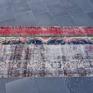 Puede incluir: Una alfombra vintage con un aspecto descolorido y desgastado. La alfombra tiene un borde rojo, blanco y azul con motivos florales. El centro de la alfombra es de color crema con un dise&ntilde;o floral descolorido.