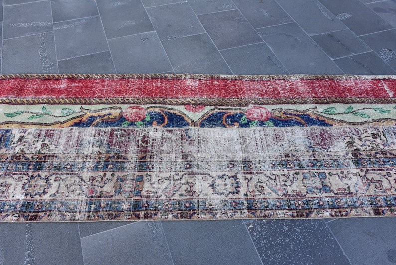 Puede incluir: Una alfombra vintage con un aspecto descolorido y desgastado. La alfombra tiene un borde rojo, blanco y azul con motivos florales. El centro de la alfombra es de color crema con un dise&ntilde;o floral descolorido.