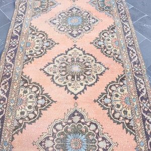 May include: A vintage rug with a peach background and intricate floral patterns in shades of brown, blue, and cream. The rug has a border with a repeating pattern.