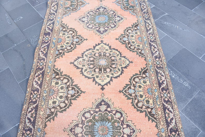 May include: A vintage rug with a peach background and intricate floral patterns in shades of brown, blue, and cream. The rug has a border with a repeating pattern.