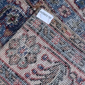 Puede incluir: Primer plano de una alfombra tejida con fondo beige y un patr&oacute;n de rayas azules, rojas y negras. La alfombra tiene una etiqueta con el texto "DCS0170".