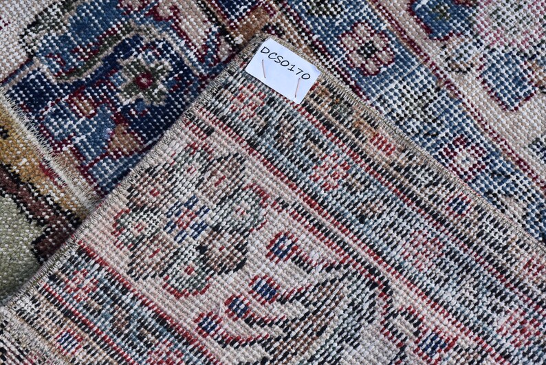 Puede incluir: Primer plano de una alfombra tejida con fondo beige y un patr&oacute;n de rayas azules, rojas y negras. La alfombra tiene una etiqueta con el texto "DCS0170".