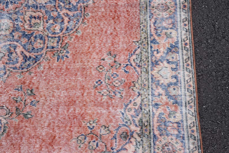 May include: Close-up of a vintage rug with a distressed, faded appearance. The rug features a central field of coral-red with intricate floral and geometric patterns in navy blue and cream. The rug's border is a darker shade of blue.