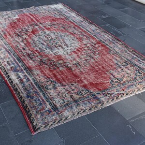 May include: A vintage red, blue, and cream colored rug with a faded floral pattern and a fringed edge.