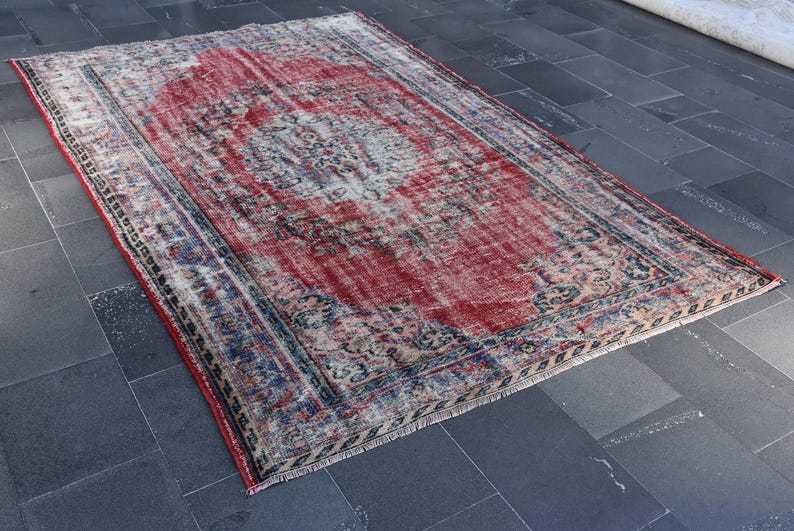 May include: A vintage red, blue, and cream colored rug with a faded floral pattern and a fringed edge.