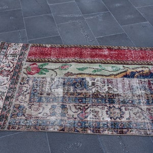 Puede incluir: Una alfombra vintage con un dise&ntilde;o de patchwork en rojo, verde, azul y crema. La alfombra tiene un patr&oacute;n floral y un borde deshilachado.