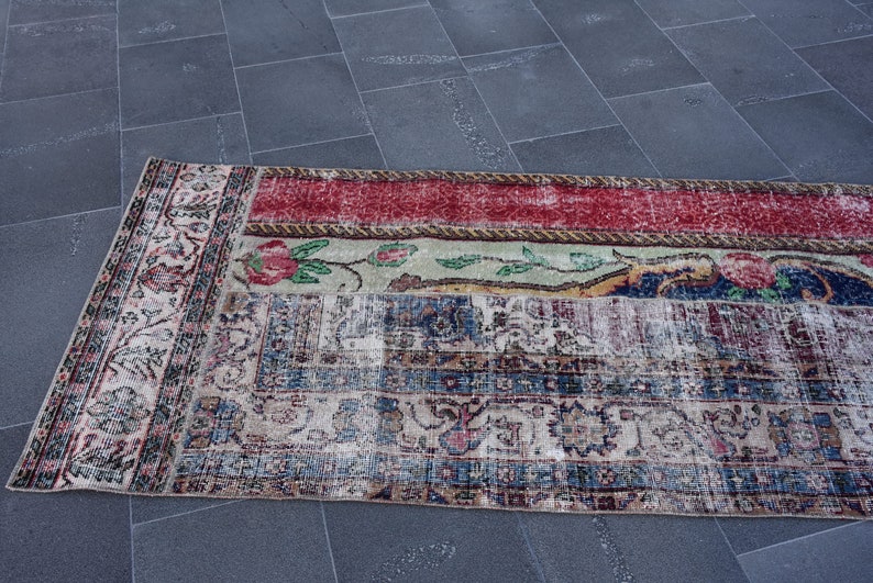 Puede incluir: Una alfombra vintage con un dise&ntilde;o de patchwork en rojo, verde, azul y crema. La alfombra tiene un patr&oacute;n floral y un borde deshilachado.