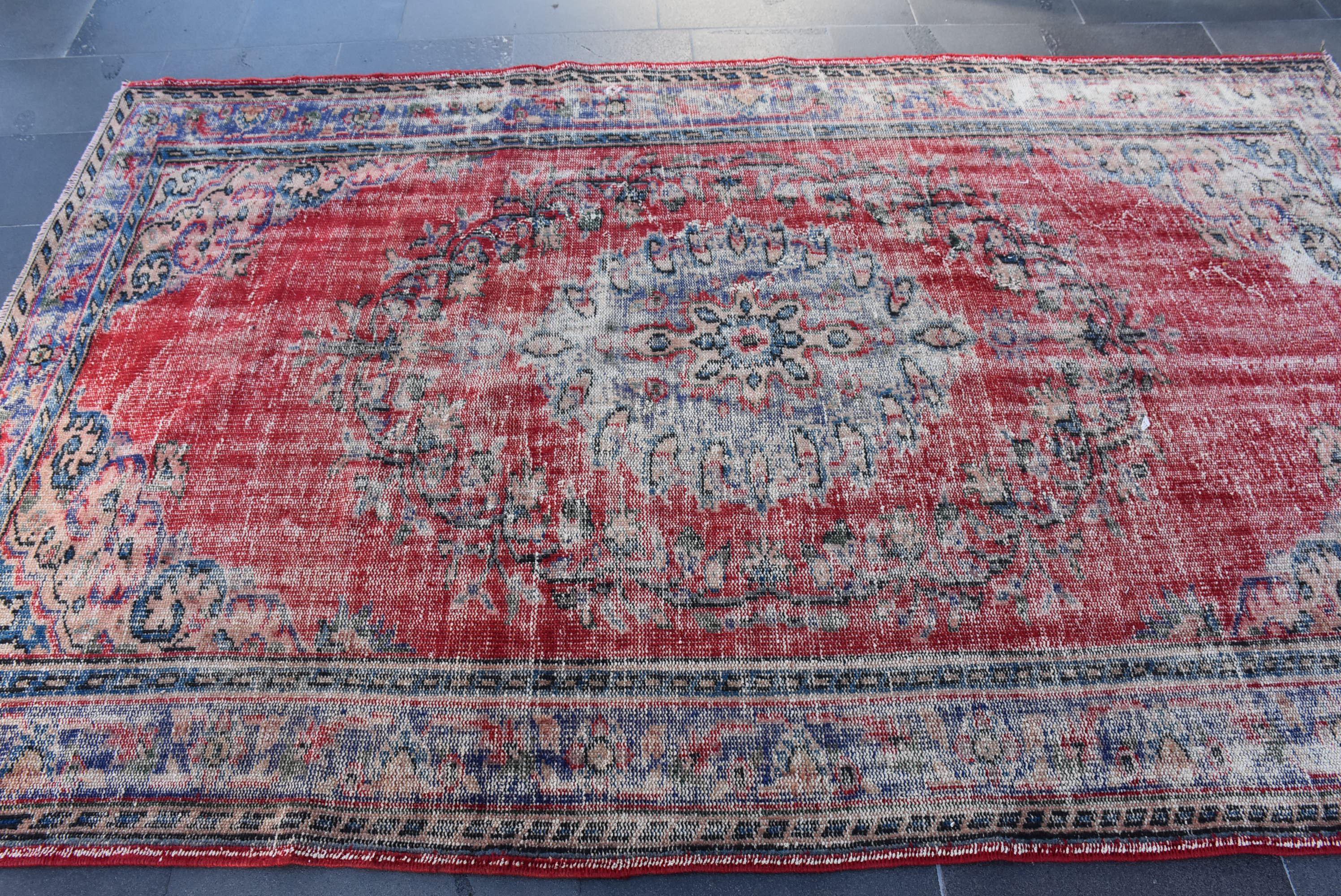 May include: A vintage red rug with a faded blue and white floral pattern. The rug has a distressed look and is made of wool.