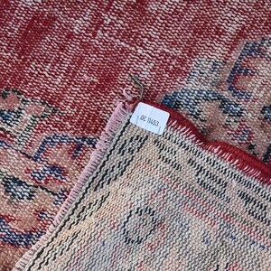 May include: Close-up of the back side of a red and blue patterned rug with a white tag that reads "DC 1453".