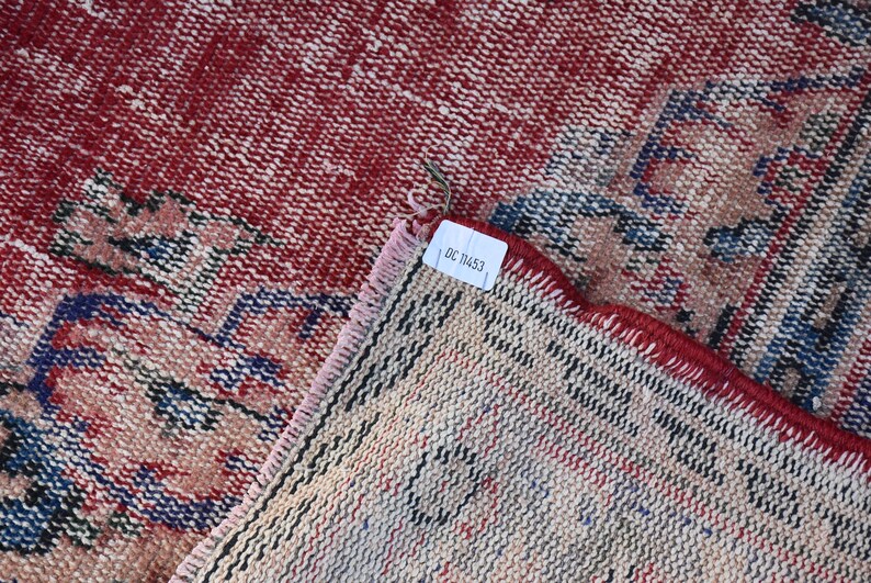 May include: Close-up of the back side of a red and blue patterned rug with a white tag that reads "DC 1453".