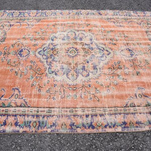 May include: A vintage rug with a faded peach background and a floral pattern in shades of blue, green, and cream. The rug has a distressed look and a worn border.