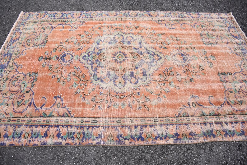 May include: A vintage rug with a faded peach background and a floral pattern in shades of blue, green, and cream. The rug has a distressed look and a worn border.