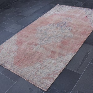 May include: A vintage rug with a faded pink and cream colour scheme. The rug has a floral pattern with a central medallion. The rug has a fringed edge.