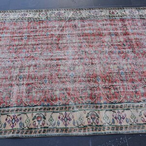 May include: A distressed, rectangular rug with a faded red and cream color palette. The rug features a central field of red with subtle patterns and a cream-colored border with floral and geometric designs. The rug's worn appearance adds to its vintage charm.