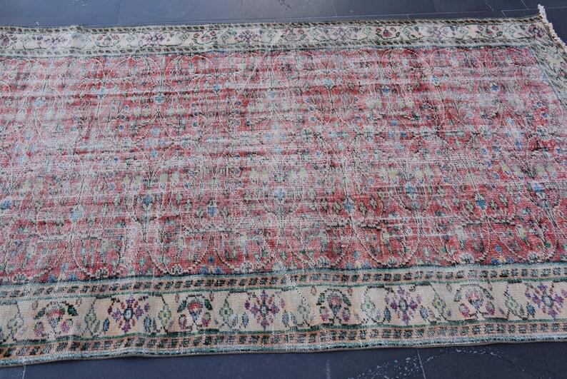 May include: A distressed, rectangular rug with a faded red and cream color palette. The rug features a central field of red with subtle patterns and a cream-colored border with floral and geometric designs. The rug's worn appearance adds to its vintage charm.