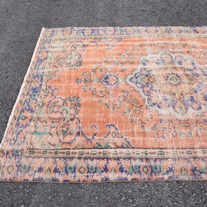 May include: A vintage rug with a peach background and a floral pattern in shades of blue, green, and cream. The rug has a distressed look and a fringed edge.