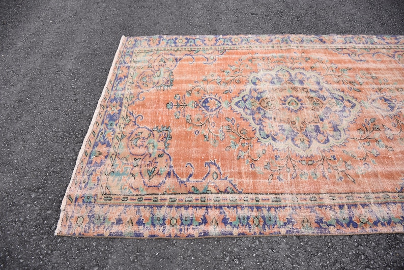 May include: A vintage rug with a peach background and a floral pattern in shades of blue, green, and cream. The rug has a distressed look and a fringed edge.