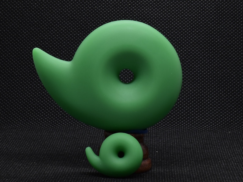 May include: Two green, abstract, spiral-shaped sculptures. The larger sculpture is the primary focus, with a smaller version of the same design below it. The sculptures are a solid, matte green color and sit on a dark background.