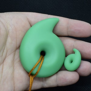 May include: Two jade green pendants, one large and one small, each with a spiral design and a central hole. The larger pendant has a gold cord. The pendants are displayed against a neutral background.
