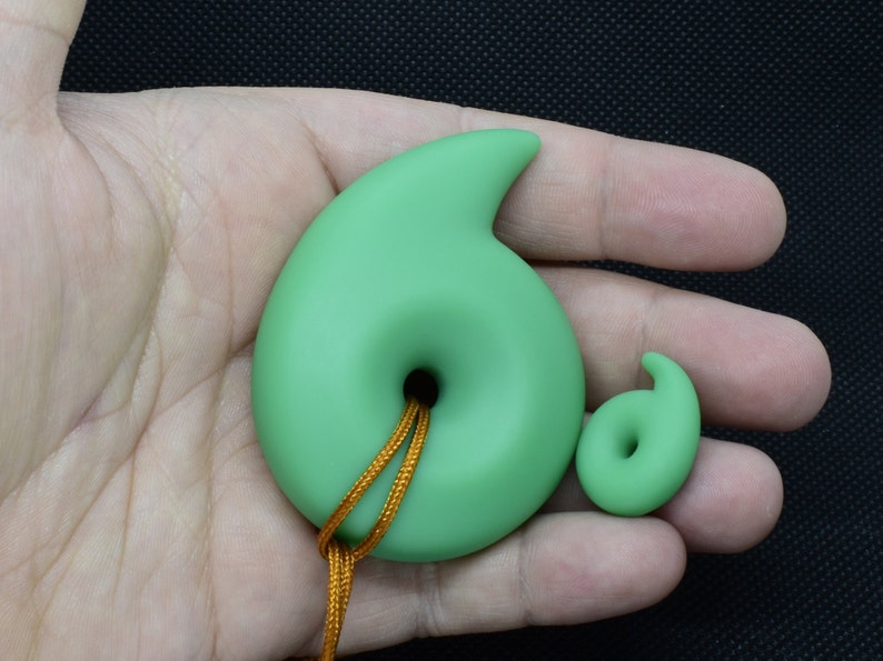 May include: Two jade green pendants, one large and one small, each with a spiral design and a central hole. The larger pendant has a gold cord. The pendants are displayed against a neutral background.