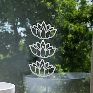 Könnte beinhalten: Ein weißes Badezimmer mit einer Badewanne und einem Fenster. Das Fenster hat ein weißes Lotusblumen-Design auf dem Glas.
