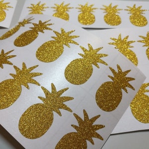 Op de afbeelding: Vellen gouden glitter ananas stickers. De stickers hebben een gedetailleerd ananasontwerp met een getextureerde, sprankelende afwerking. De stickers staan op een witte achtergrond en zijn ideaal voor knutselen of decoreren.