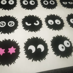 May include: Sheet of black, round, fuzzy stickers with various white eye designs and two pink star-shaped eyes. The stickers are arranged in rows and columns on a white background.