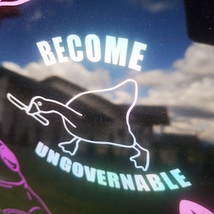 Puede incluir: Una pegatina blanca sobre un fondo negro con un pato de dibujos animados sosteniendo un cuchillo y el texto "Become Ungovernable".