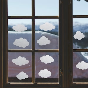 May include: A wooden window frame with multiple panes, each adorned with white cloud-shaped decals. The background shows a snowy landscape, creating a whimsical, weather-themed decorative effect. The window is divided into multiple panes.