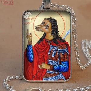 Puede incluir: Collar con colgante de plata antigua. El colgante rectangular presenta una ilustraci&oacute;n de una figura con cabeza de perro, vestida con una capa roja y sosteniendo una lanza. El colgante tiene el texto "CHRISTOPHER". El collar es de cadena de plata.