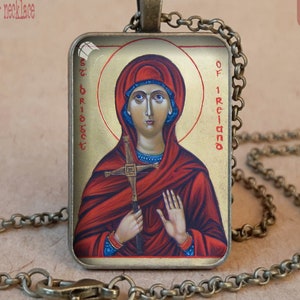 Puede incluir: Collar con colgante de bronce antiguo con un icono religioso de Santa Br&iacute;gida de Irlanda. El colgante rectangular muestra un retrato de una mujer en tonos rojos y dorados, sosteniendo una cruz. La cadena y el bisel son de bronce antiguo.