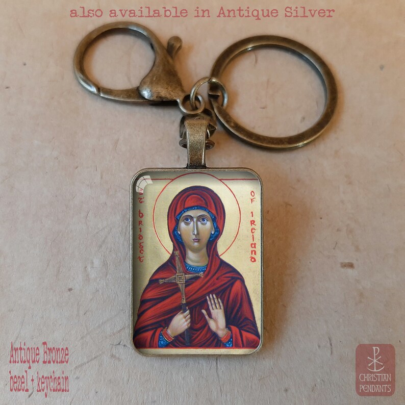 Puede incluir: Llavero de bronce antiguo con un colgante cuadrado con un icono religioso. El icono representa a una mujer en rojo y oro con el texto "St. Bridget of Ireland". El llavero tiene un cierre de mosquet&oacute;n y un llavero.