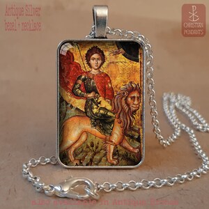 May include: Antique silver bezel necklace featuring a religious icon of a figure riding a lion. The rectangular pendant has a detailed image with red, gold, and green hues. The chain is a silver-colored, linked design.