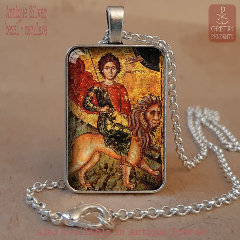 May include: Antique silver bezel necklace featuring a religious icon of a figure riding a lion. The rectangular pendant has a detailed image with red, gold, and green hues. The chain is a silver-colored, linked design.