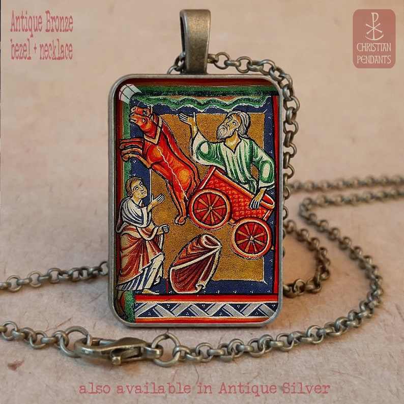 Pode incluir: Colar com moldura em bronze antigo e pingente retangular com uma ilustra&ccedil;&atilde;o religiosa colorida. O pingente mostra figuras com uma carruagem puxada por cavalos. A corrente e o fecho tamb&eacute;m s&atilde;o em bronze antigo. O texto "Antique Bronze bezel + necklace" &eacute; vis&iacute;vel.