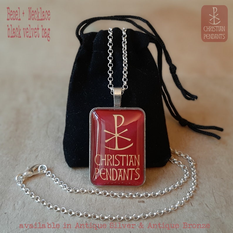 May include: A silver-toned necklace with a rectangular pendant featuring a red background and gold text that reads "CHRISTIAN PENDANTS". The pendant displays a Chi-Rho symbol. The necklace is displayed with a black velvet bag.