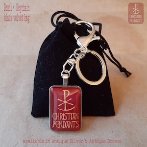 May include: A red and silver keychain pendant featuring the text "CHRISTIAN PENDANTS" and a religious symbol. The keychain is attached to a silver clasp and a key ring. It is presented with a black velvet bag.