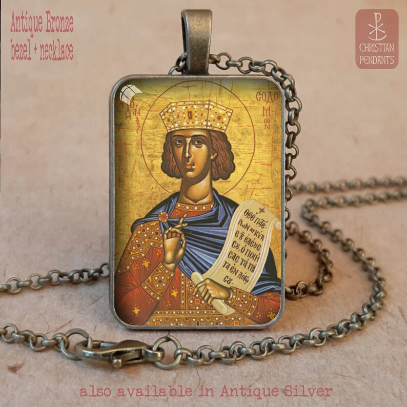 May include: Antique bronze pendant necklace featuring a religious icon with a gold halo and crown. The rectangular pendant displays a figure holding a scroll. The necklace has a chain and clasp. The text "CHRISTIAN PENDANTS" is visible.
