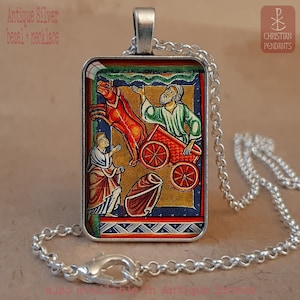 Pode incluir: Colar com pingente retangular de prata antiga. O pingente apresenta uma ilustra&ccedil;&atilde;o medieval colorida com figuras e uma carro&ccedil;a puxada por cavalos. A corrente prateada tem um design de elos e um fecho de lagosta. O texto "Christian Pendants" &eacute; vis&iacute;vel.